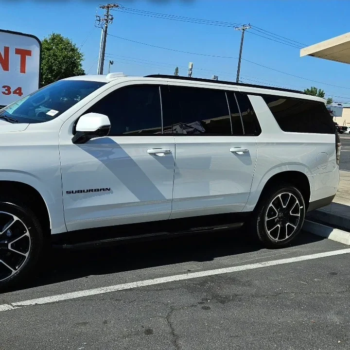 White 2024 Chevrolet Suburban with freshly tinted windows, beside the King Window Tint sign on Fulton Ave, Sacramento