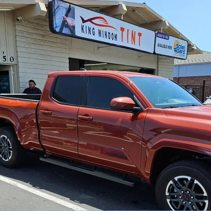 Orange 2024 Toyota Tacoma with freshly tinted windows, beside the King Window Tint sign on Fulton Ave, Sacramento