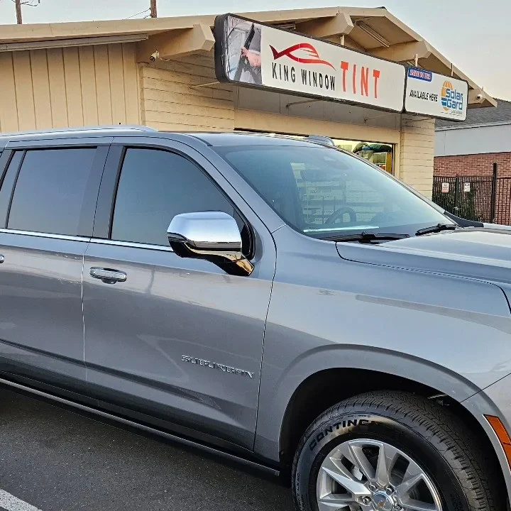Silver 2025 Chevrolet Suburban with freshly tinted windows, beside the King Window Tint sign on Fulton Ave, Sacramento