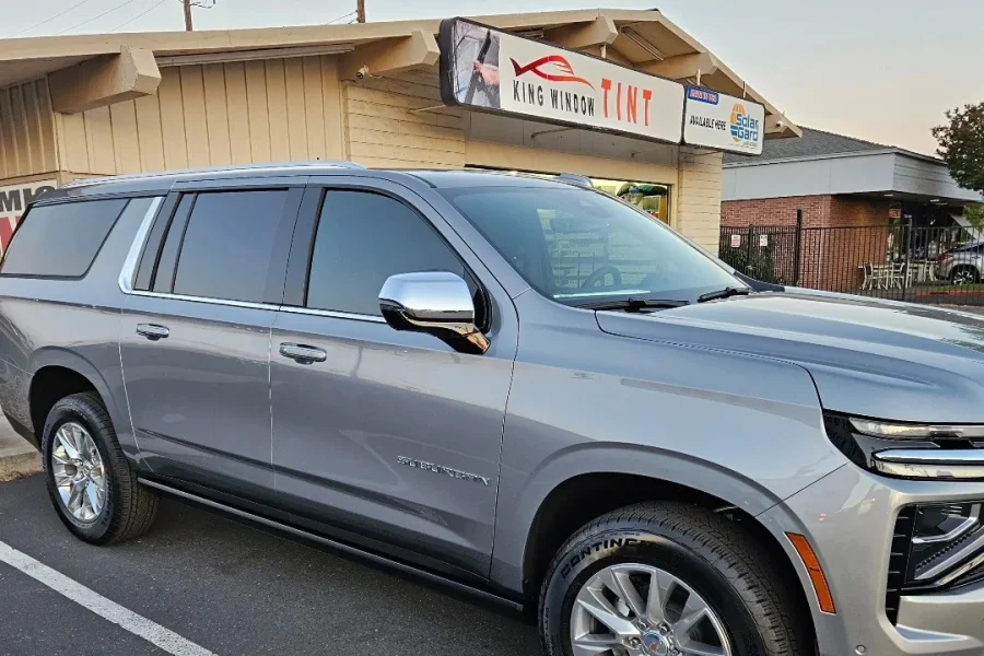 Silver 2025 Chevrolet Suburban with freshly tinted windows, beside the King Window Tint sign on Fulton Ave, Sacramento