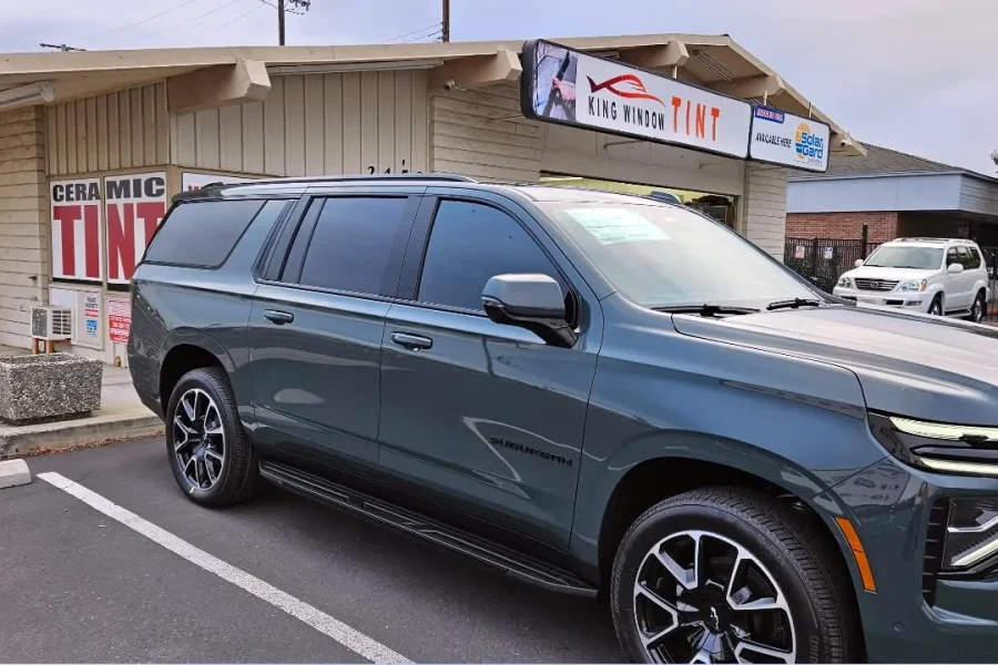Dark green-gray 2025 Chevrolet Suburban with freshly tinted windows, outside the King Window Tint shop on Fulton Ave in Sacramento