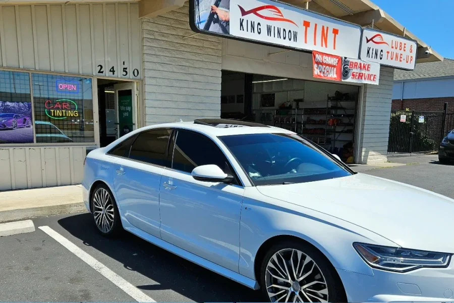 White Audi A6 with freshly tinted windows, beside the King Window Tint sign on Fulton Ave, Sacramento