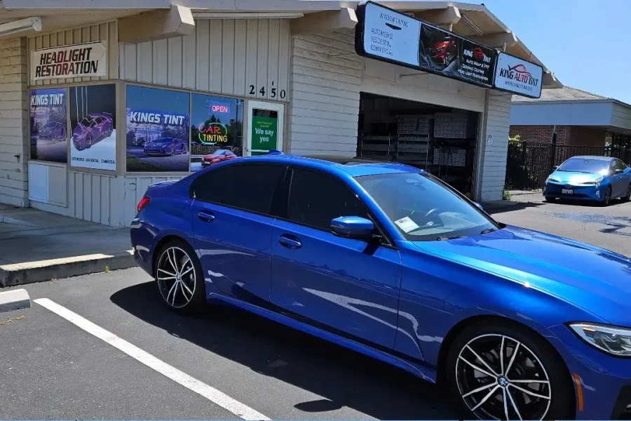 Blue BMW 3 Series with freshly tinted windows, beside the King Auto Tint sign on Fulton Ave, Sacramento