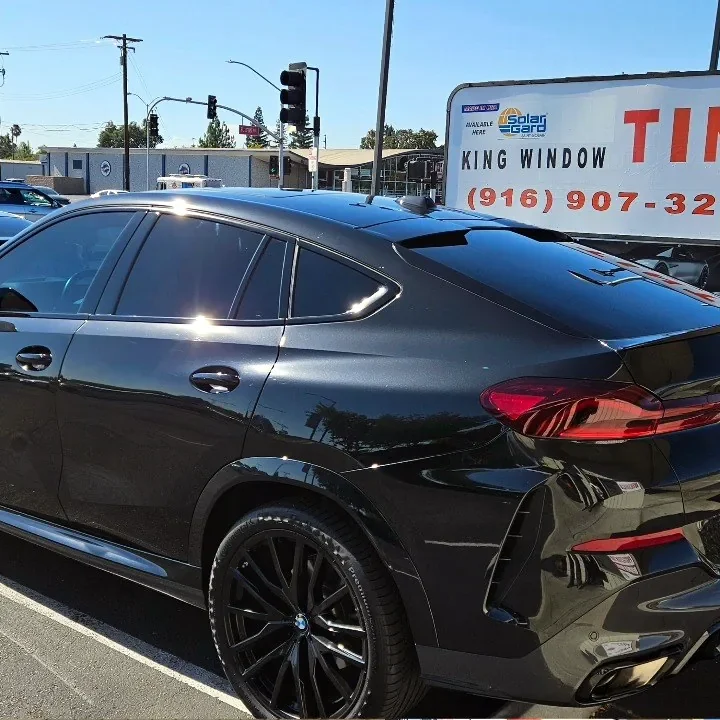 Black BMW X6 with freshly tinted windows, beside the King Window Tint sign on Fulton Ave, Sacramento