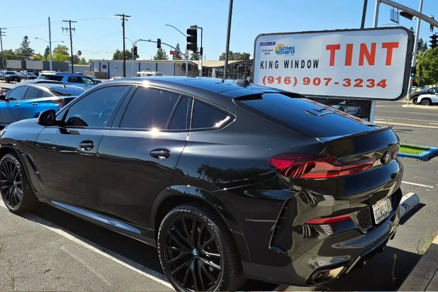 Black BMW X6 with freshly tinted windows, beside the King Window Tint sign on Fulton Ave, Sacramento