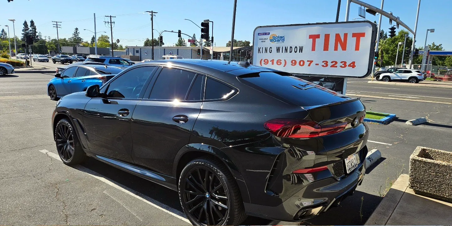 Black BMW X6 with freshly tinted windows, beside the King Window Tint sign on Fulton Ave, Sacramento