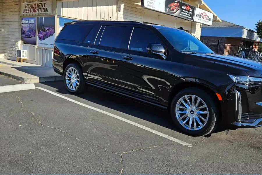 Black Cadillac Escalade ESV with freshly tinted windows, beside the King Auto Tint sign on Fulton Ave, Sacramento