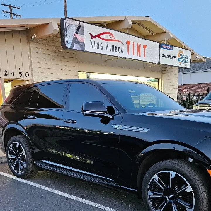 Black Cadillac Escalade IQ with freshly tinted windows, beside the King Window Tint sign on Fulton Ave, Sacramento
