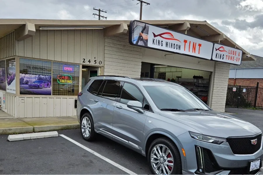 Gray Cadillac XT6 with freshly tinted windows, beside the King Window Tint sign on Fulton Ave, Sacramento
