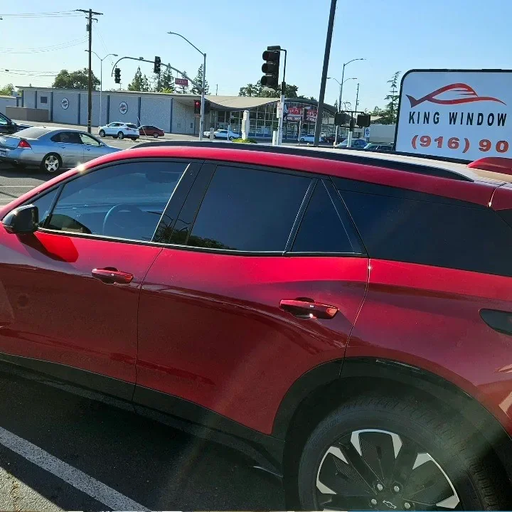Red Chevrolet Blazer EV with freshly tinted windows, beside the King Window Tint sign on Fulton Ave, Sacramento