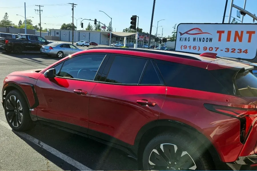 Red Chevrolet Blazer EV with freshly tinted windows, beside the King Window Tint sign on Fulton Ave, Sacramento