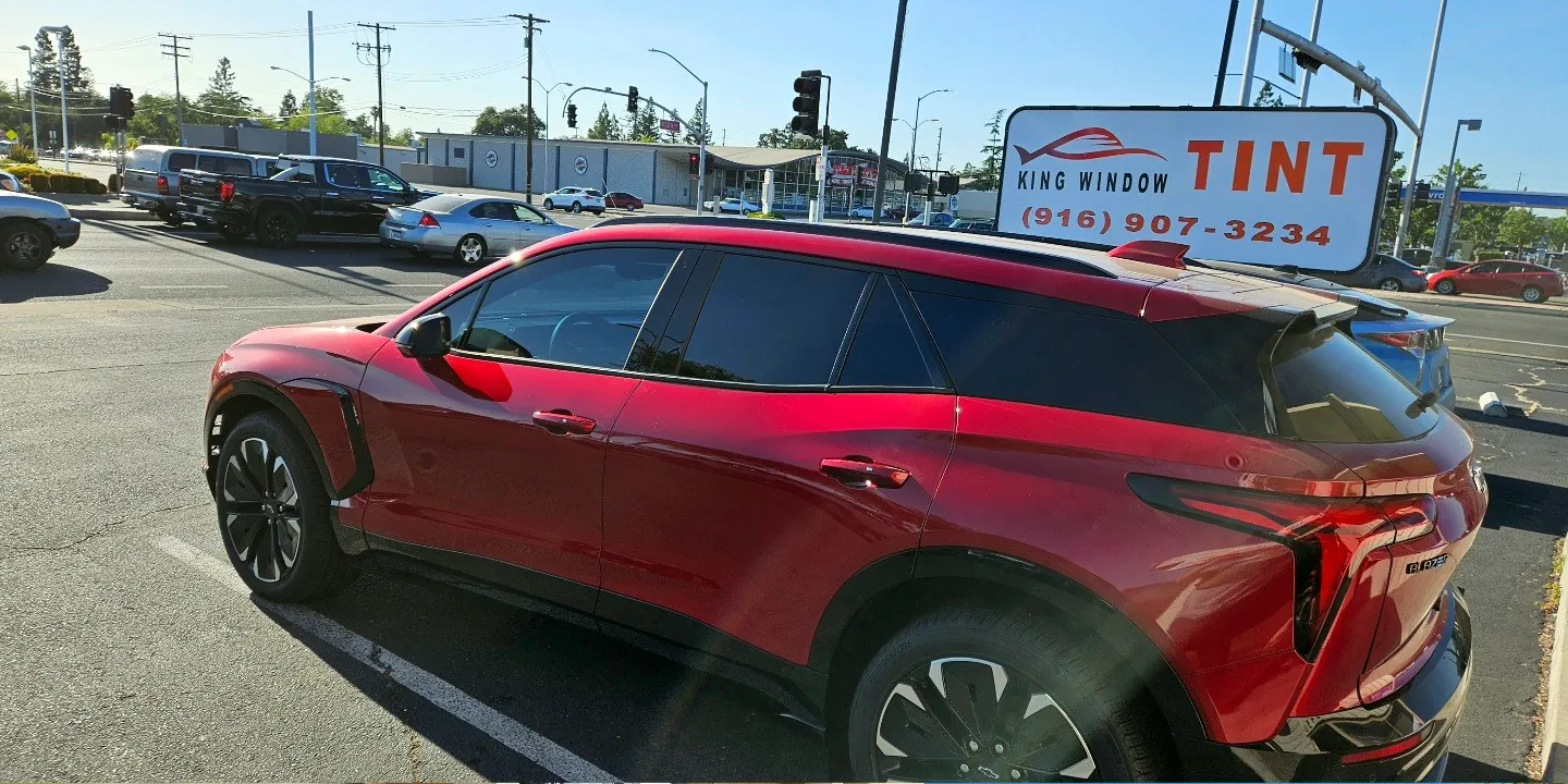 Red Chevrolet Blazer EV with freshly tinted windows, beside the King Window Tint sign on Fulton Ave, Sacramento
