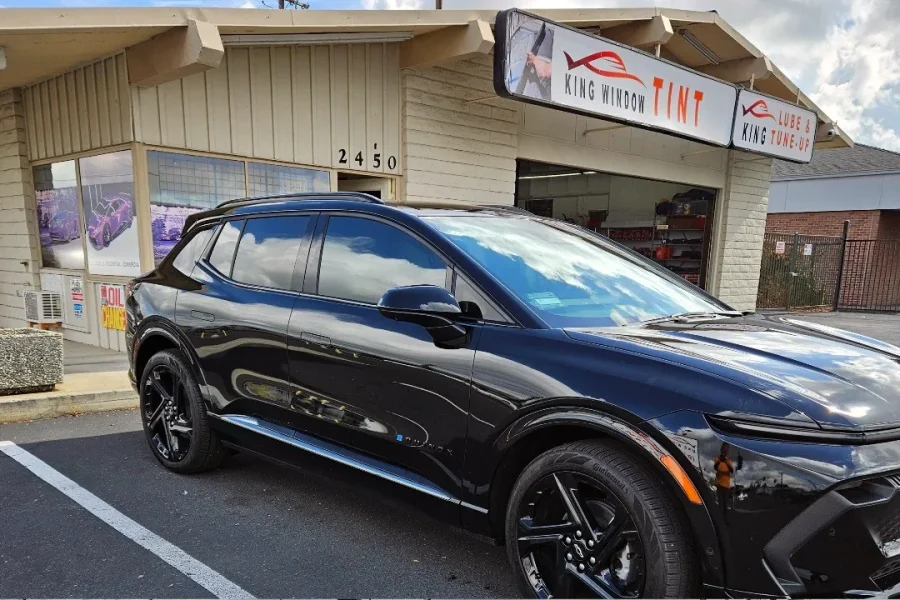Black Chevrolet Equinox EV with freshly tinted windows, beside the King Window Tint sign on Fulton Ave, Sacramento
