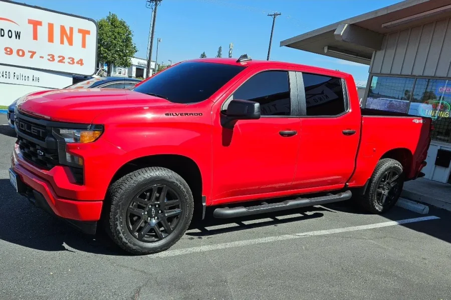 Red Chevrolet Silverado 1500 with freshly tinted windows, beside the King Window Tint sign on Fulton Ave, Sacramento