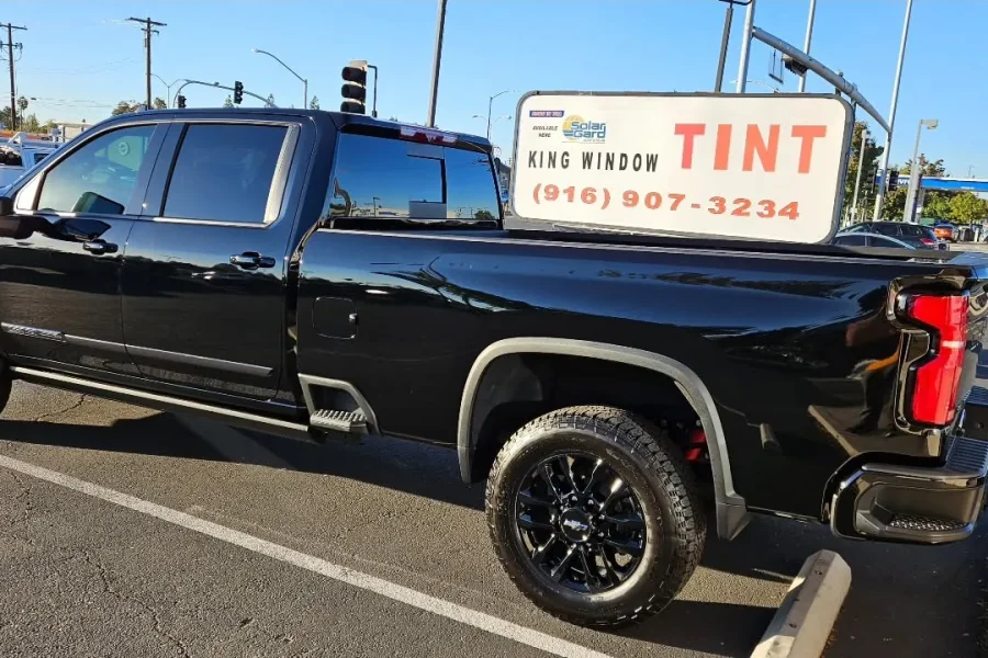 Black Chevrolet Silverado 3500HD with freshly tinted windows, beside the King Window Tint sign on Fulton Ave, Sacramento