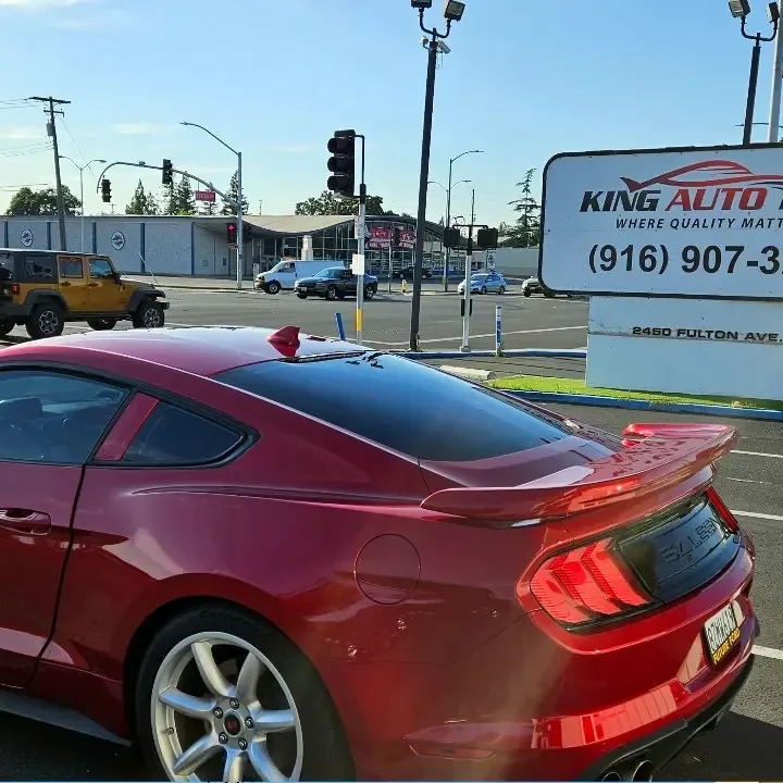 Red Ford Mustang GT with freshly tinted windows, beside the King Auto Tint sign on Fulton Ave, Sacramento