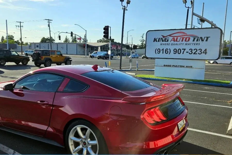 Red Ford Mustang GT with freshly tinted windows, beside the King Auto Tint sign on Fulton Ave, Sacramento