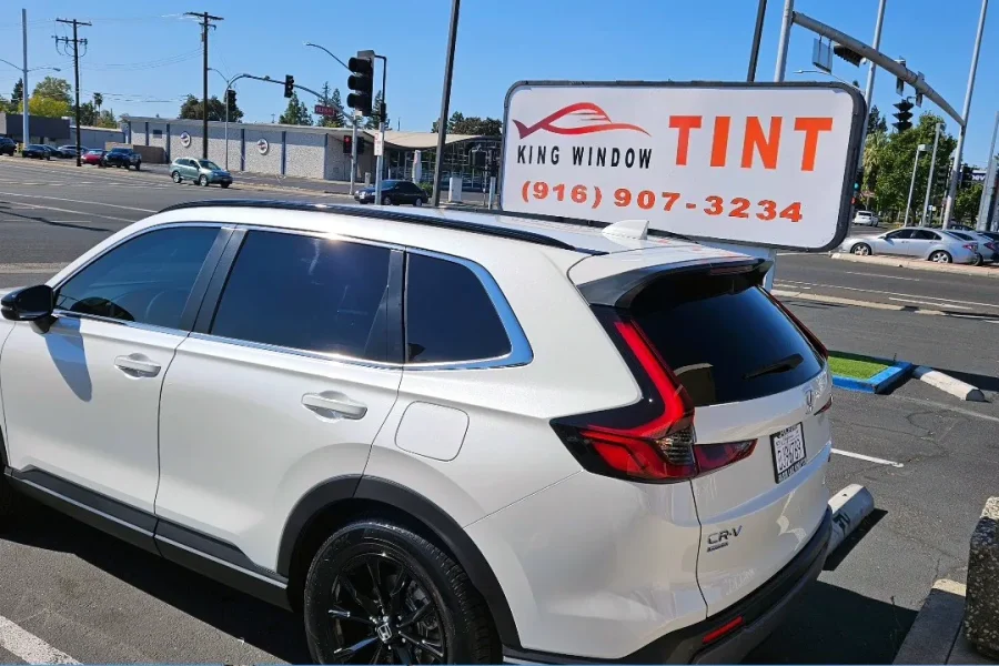 White Honda CR-V with freshly tinted windows, beside the King Window Tint sign on Fulton Ave, Sacramento