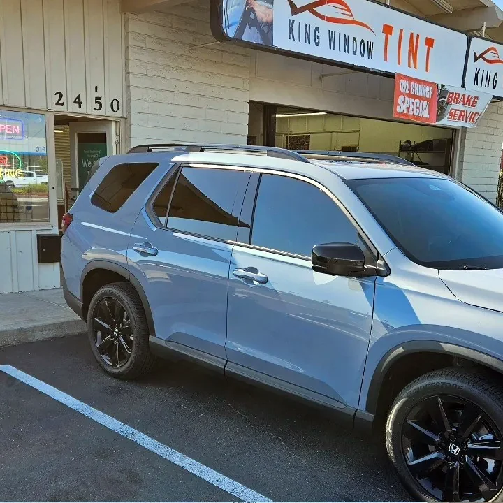 Silver blue Honda Pilot with freshly tinted windows, beside the King Window Tint sign on Fulton Ave, Sacramento