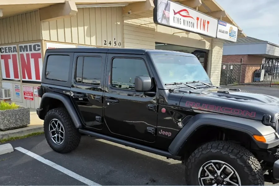 Black Jeep Wrangler Rubicon with freshly tinted windows, beside the King Window Tint sign on Fulton Ave, Sacramento