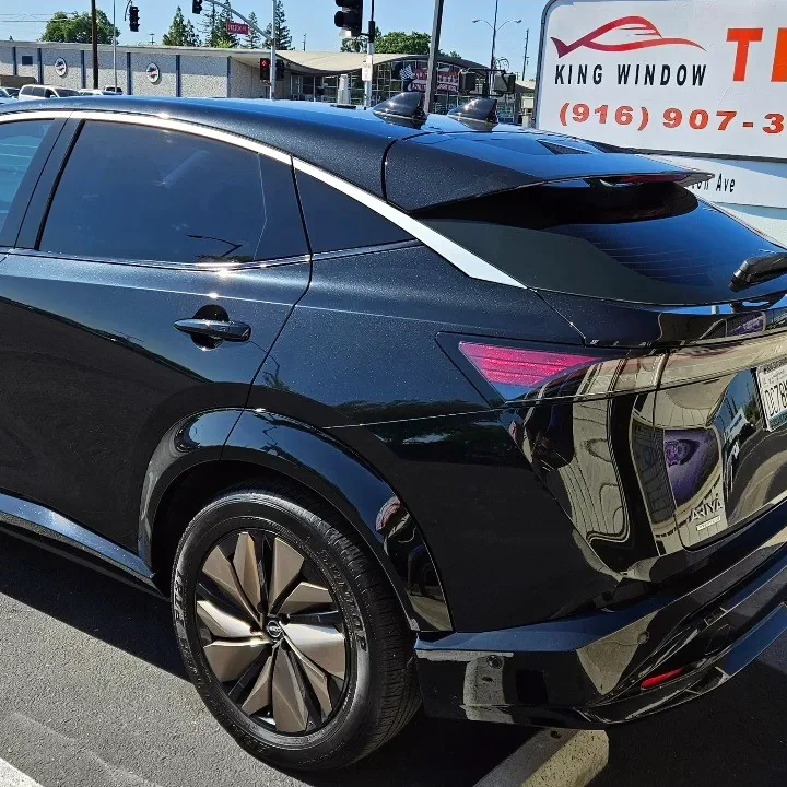 Black Nissan Ariya with freshly tinted windows, beside the King Window Tint sign on Fulton Ave, Sacramento