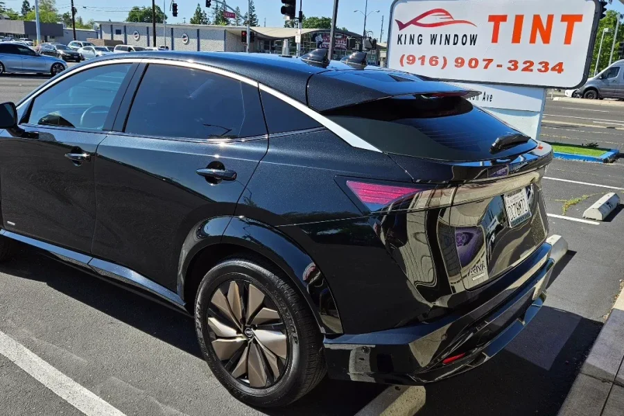 Black Nissan Ariya with freshly tinted windows, beside the King Window Tint sign on Fulton Ave, Sacramento
