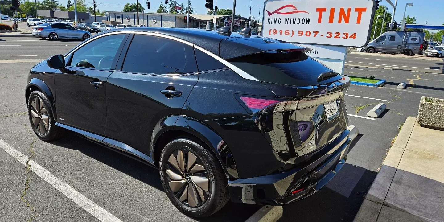 Black Nissan Ariya with freshly tinted windows, beside the King Window Tint sign on Fulton Ave, Sacramento