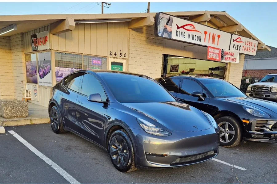 Black Porsche Macan with freshly tinted windows, outside the King Window Tint shop on Fulton Ave in Sacramento (shown with a gray Tesla Model Y)