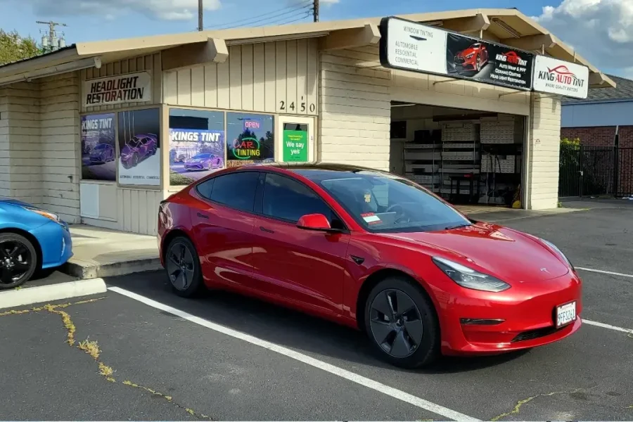 Red Tesla Model 3 with freshly tinted windows, beside the King Auto Tint sign on Fulton Ave, Sacramento