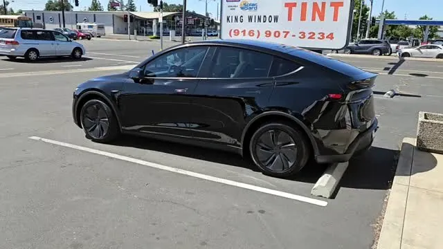 Black Tesla Model Y with freshly tinted windows, beside the King Window Tint sign on Fulton Ave, Sacramento