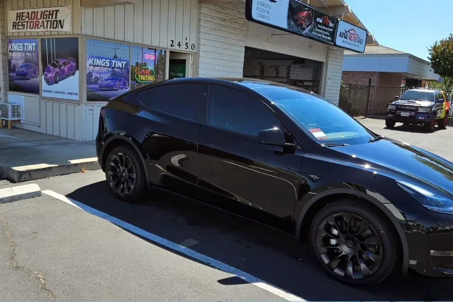 Black Tesla Model Y with freshly tinted windows, beside the King Auto Tint sign on Fulton Ave, Sacramento