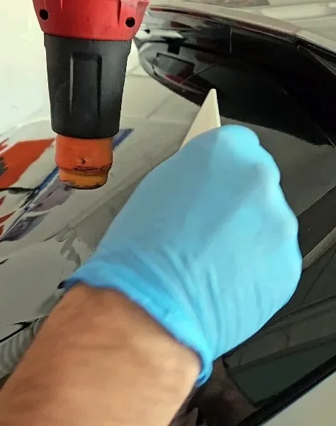 Gloved hand heat-shrinking tint film to the curve of a rear windshield with a heat gun