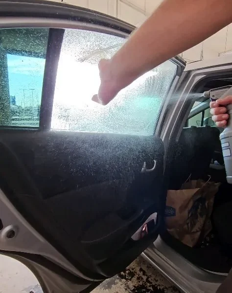 Installer spraying slip solution on an open car door window before applying tint film