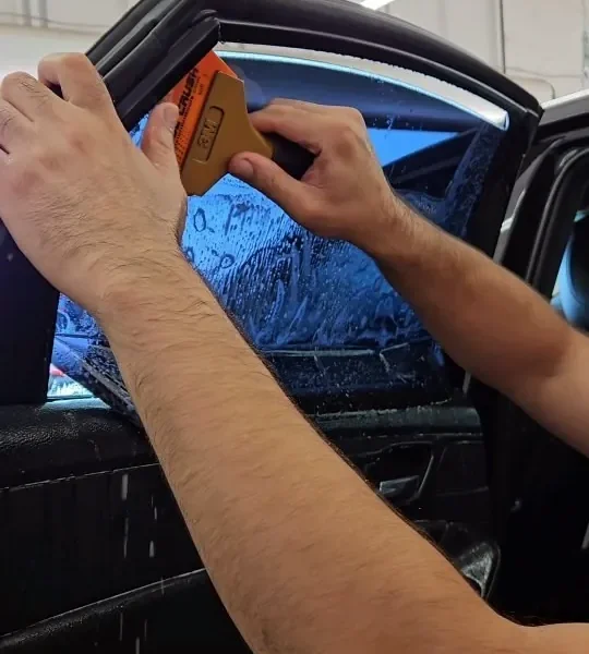 Installer squeegeeing window film onto a car door glass inside King Auto Tint in Sacramento